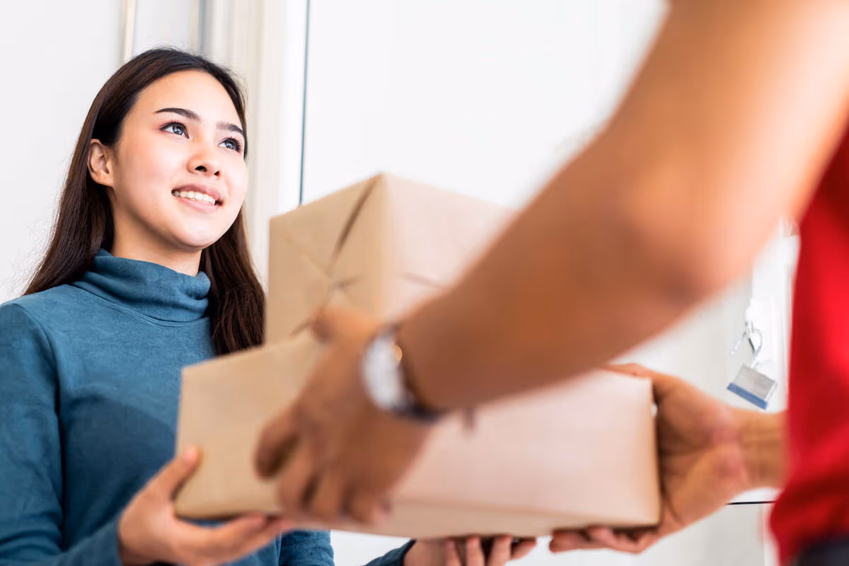 Woman in blue sweater smiles as she receives two packages from a person in red, conveying friendliness and satisfaction.